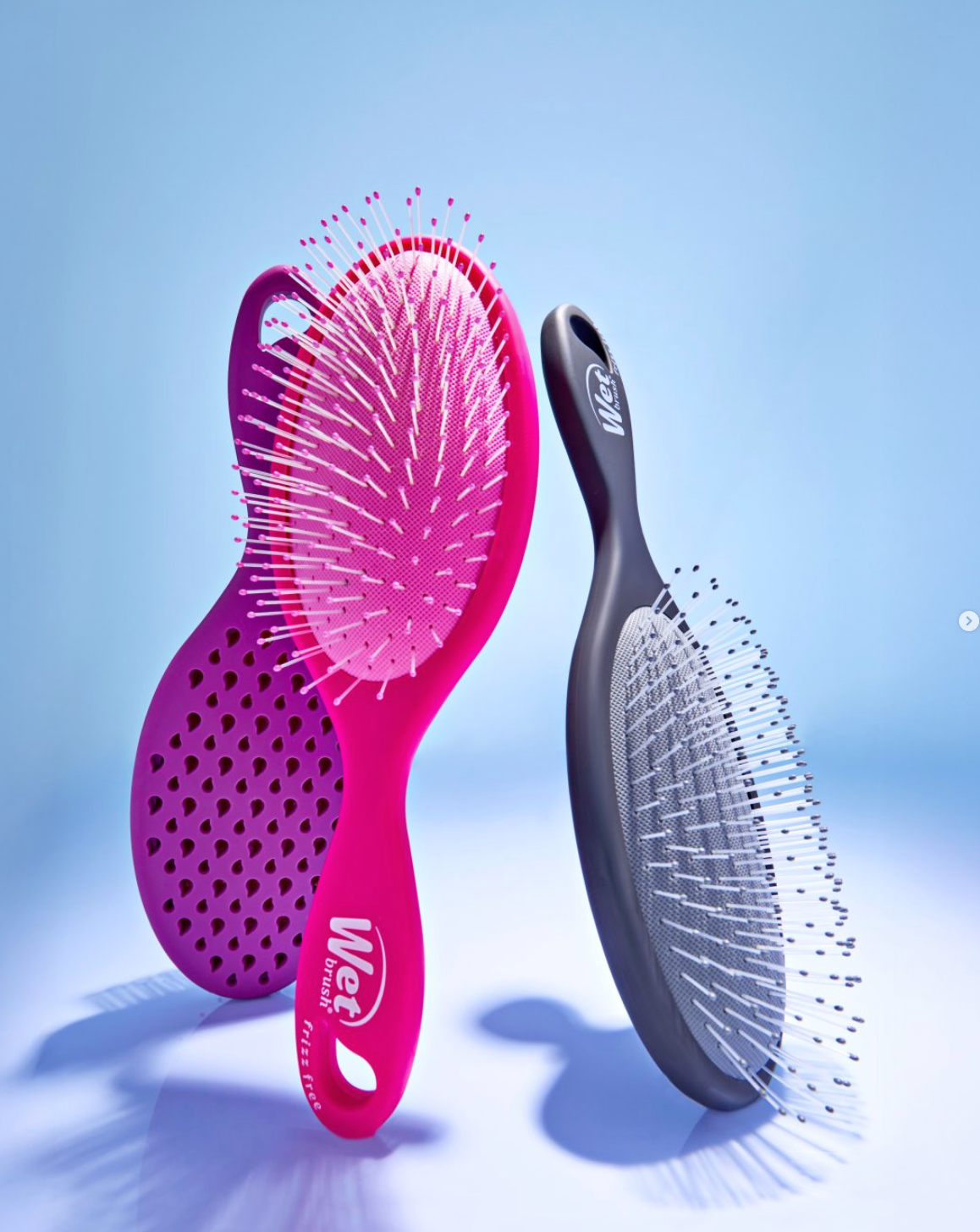 Pink and charcoal Wet Brush hairbrushes against a pale blue background